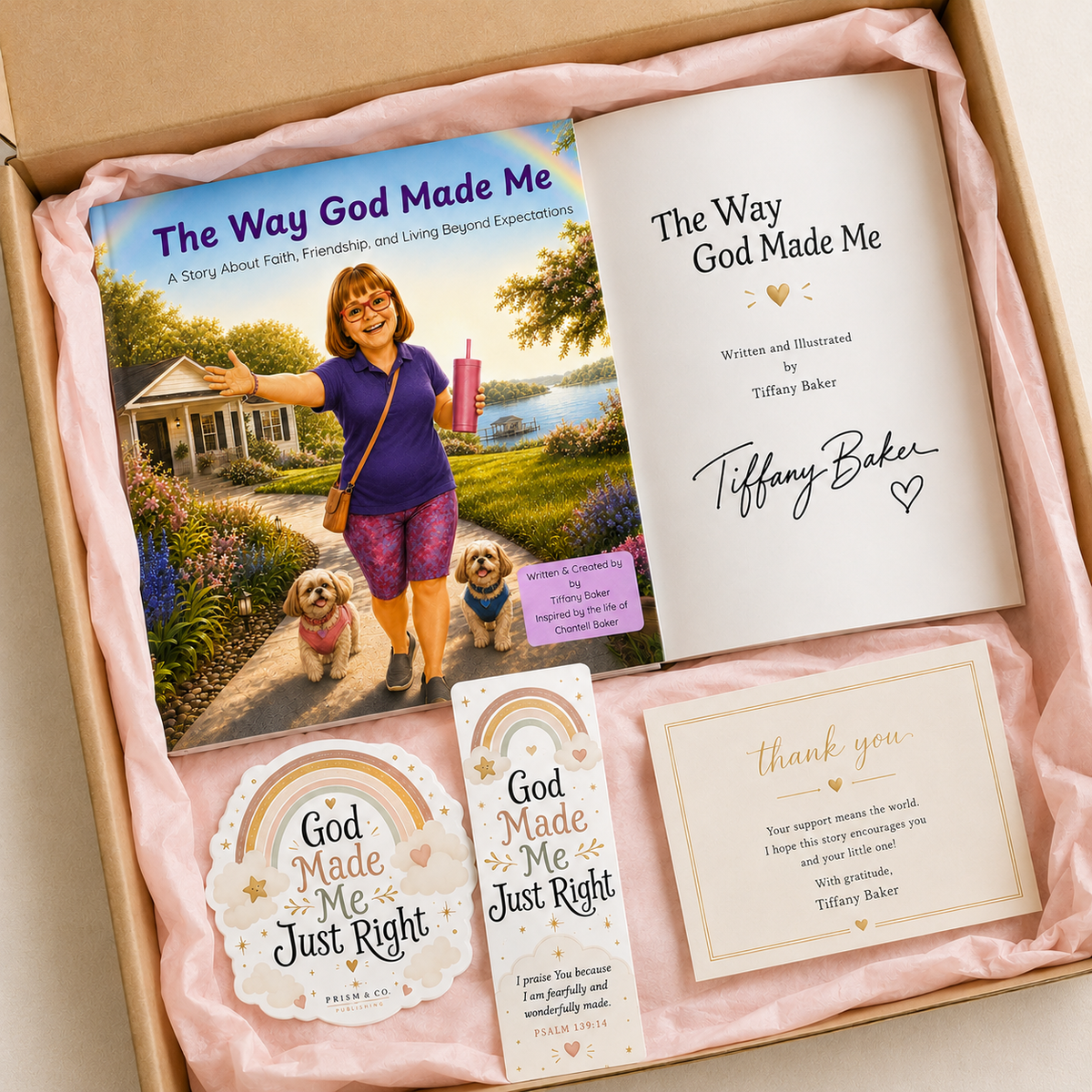 A gift box containing a book titled 'The Way God Made Me' with its printed cover and interior page, plus matching printed cards and stickers. The items are arranged on pink tissue paper inside an open cardboard box.